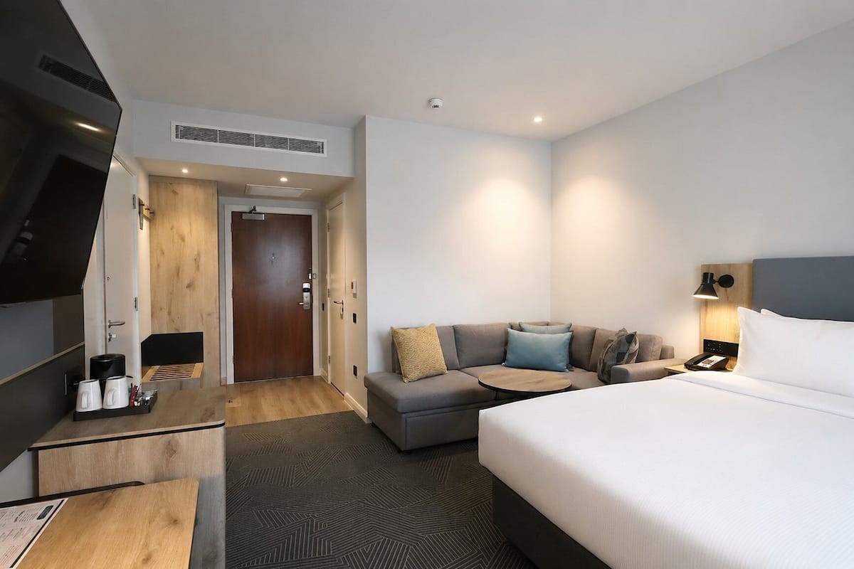 A hotel room with a bed, a sofa, a desk, a TV, and a door.