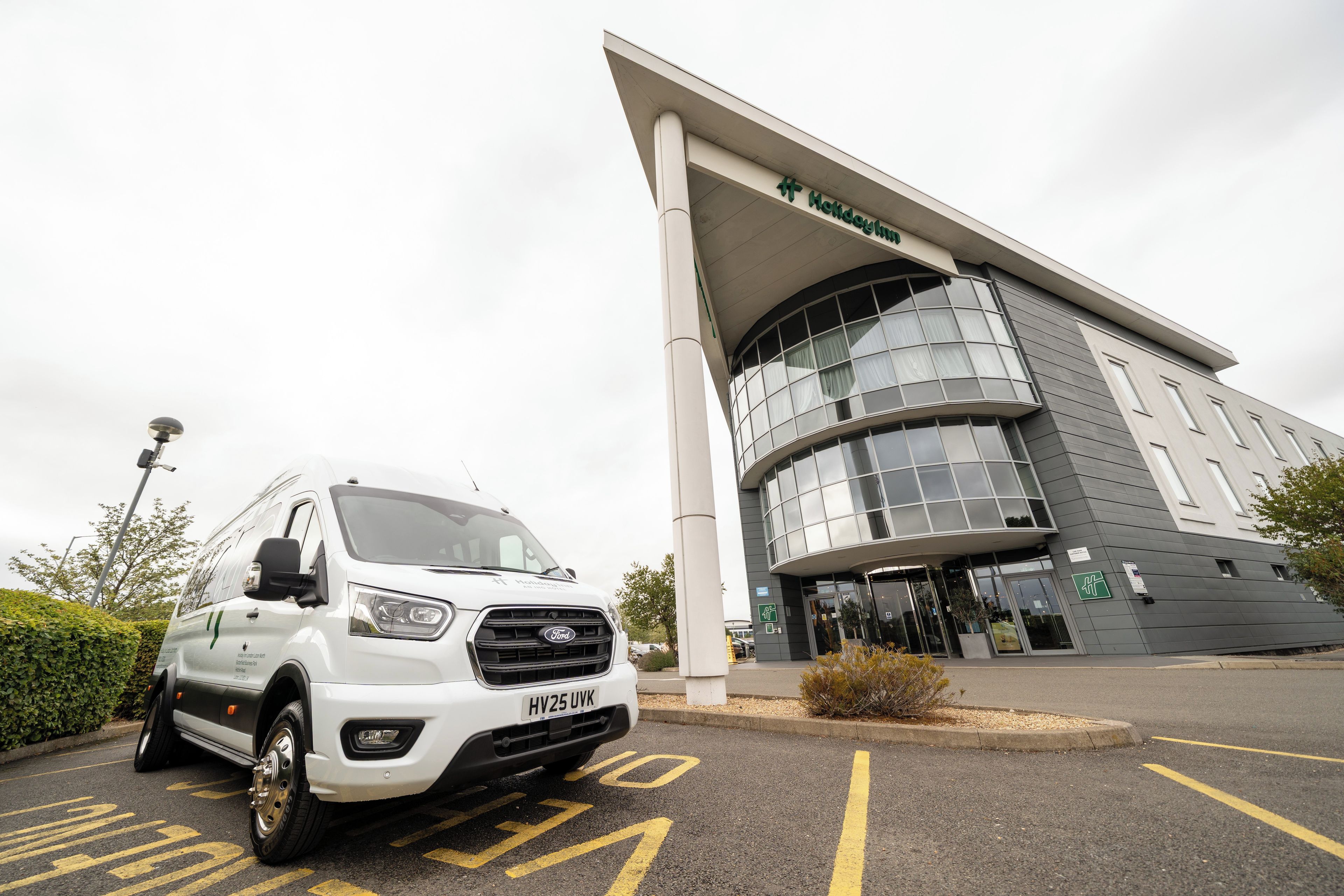 Een witte Ford bestelwagen geparkeerd voor een gebouw met een grote glazen ingang en een bord waarop 'Holiday Inn Express' staat.