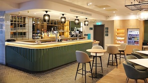 Una zona de bar con mostrador, taburetes y un refrigerador lleno de bebidas.