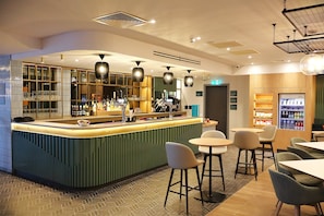 A bar area with a counter, stools, and a refrigerator stocked with beverages. - Holiday Inn London Luton North (Luton)