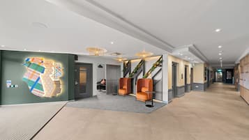 Un moderno vestíbulo de hotel con un largo pasillo, zona de estar con sillones naranjas y un gran mural en la pared.