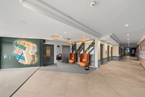 A modern hotel lobby with a long corridor, seating area with orange chairs, and a large wall mural. - Holiday Inn London Luton North by IHG (Luton)