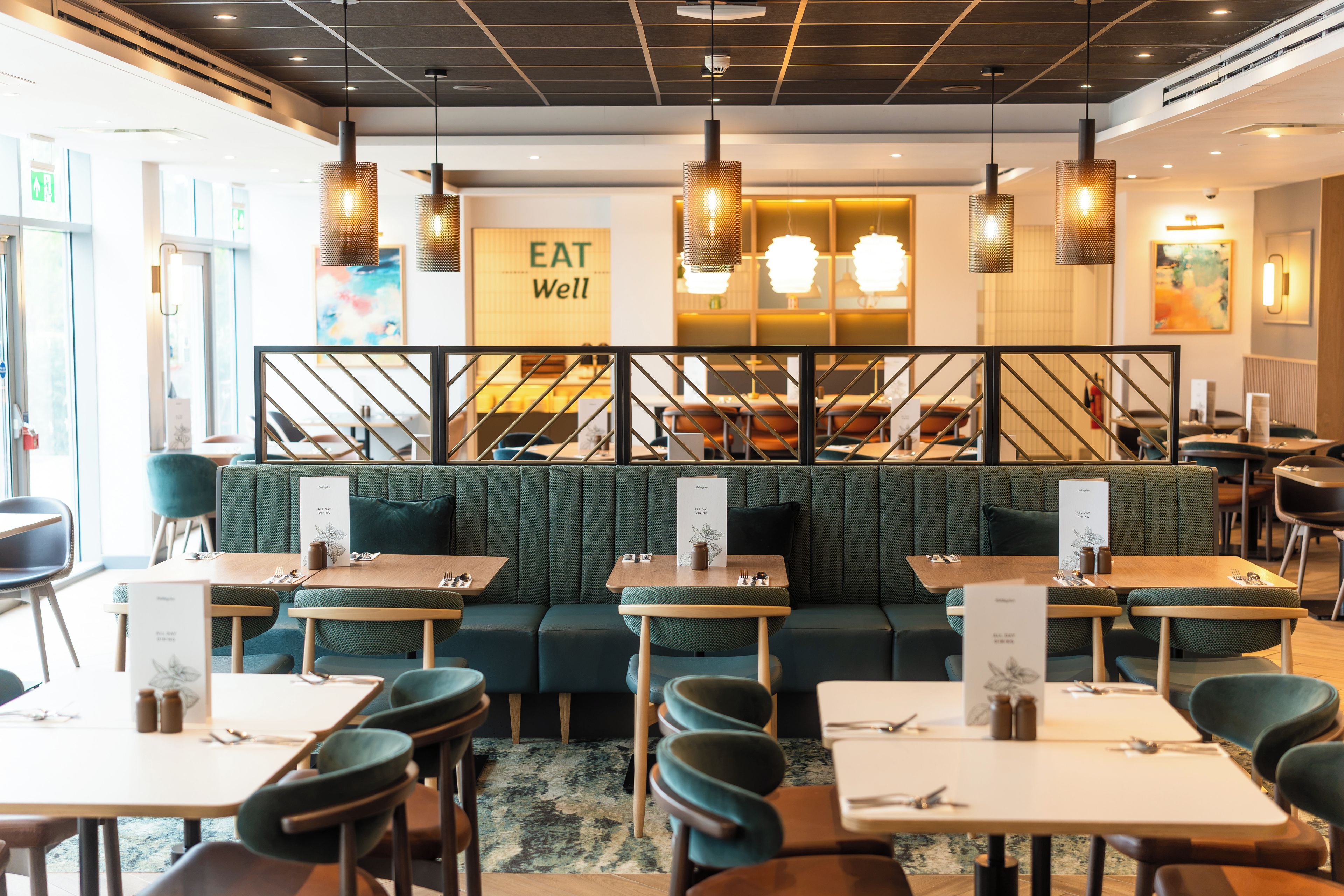 A restaurant interior with green upholstered booths, wooden tables, and hanging pendant lights.