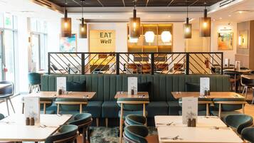 A restaurant interior with green upholstered booths, wooden tables, and hanging pendant lights.