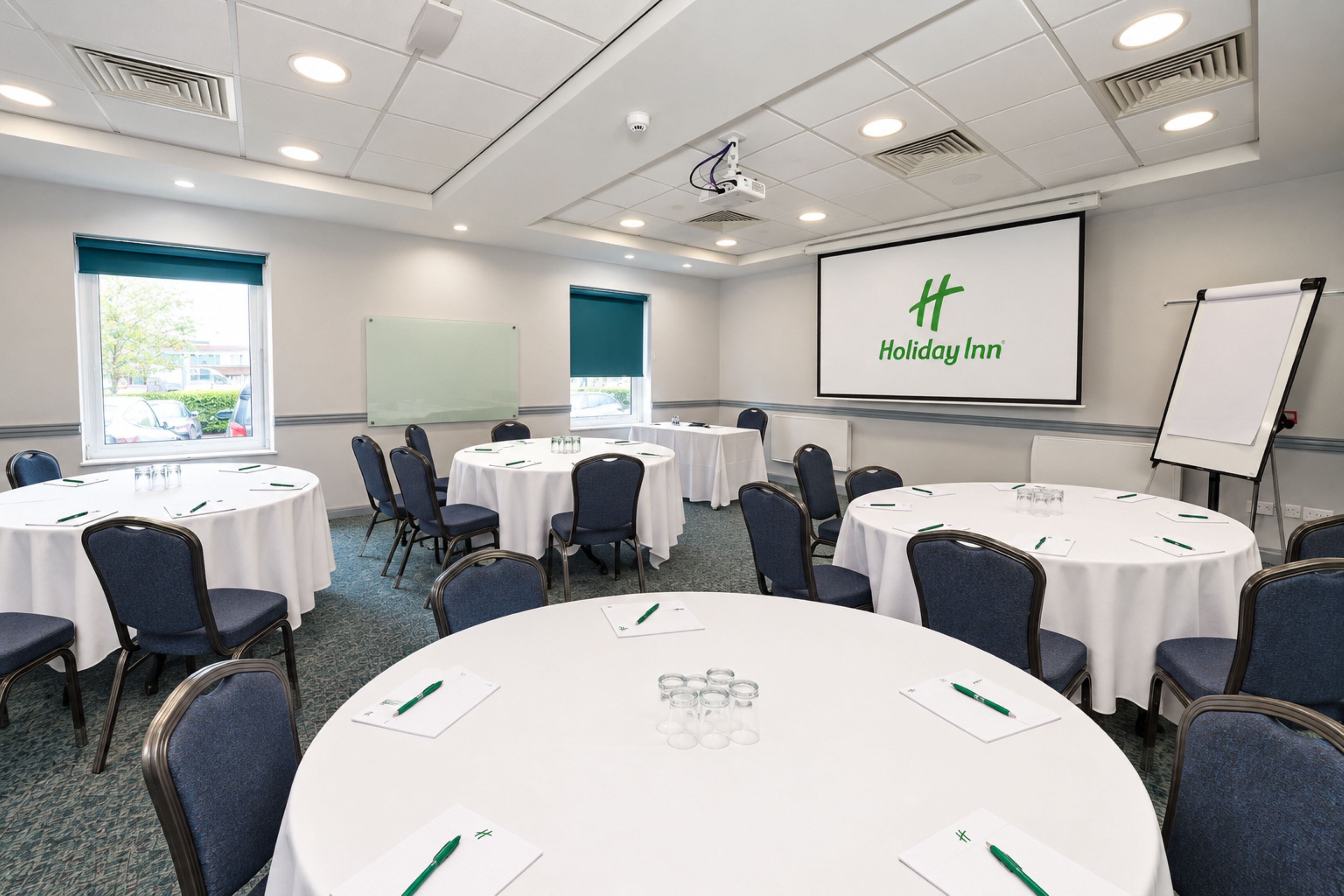 A conference room with round tables, chairs, a projector screen, and a whiteboard.