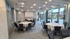 A conference room with round tables, chairs, a projector screen, and a whiteboard. - London Luton Vale Hotel (Luton)