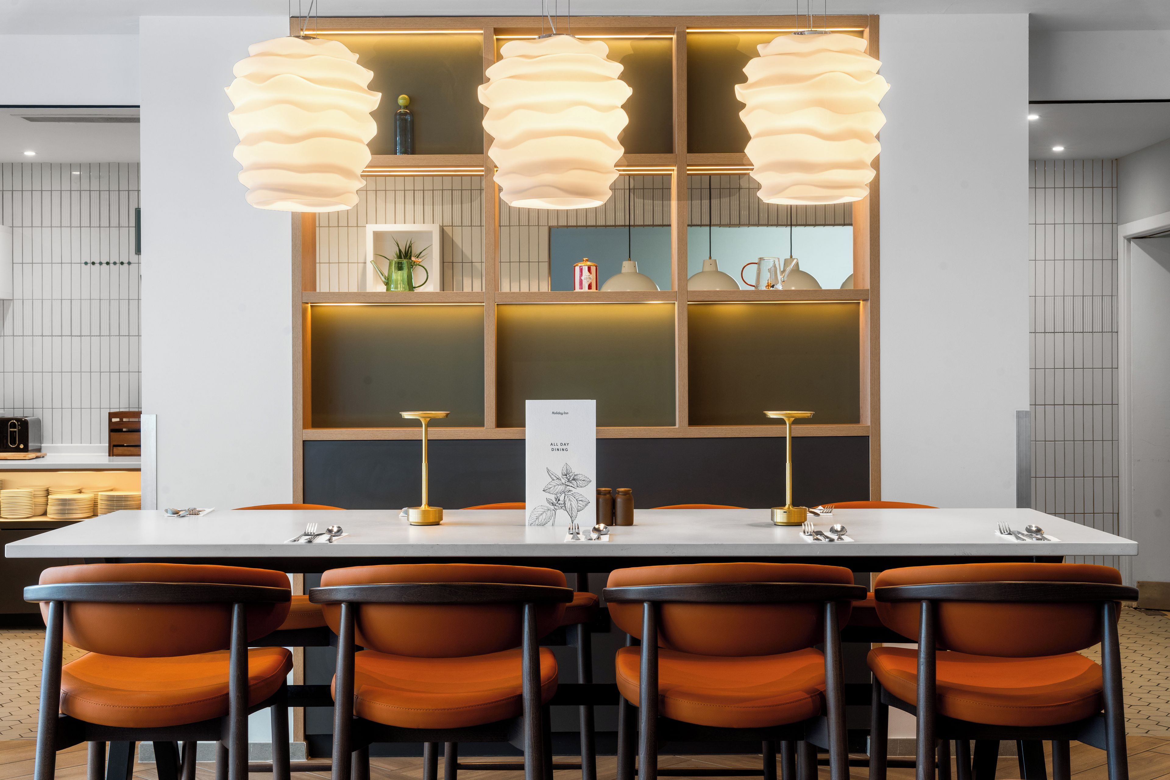 A modern dining area with a white table, orange chairs, and pendant lights.