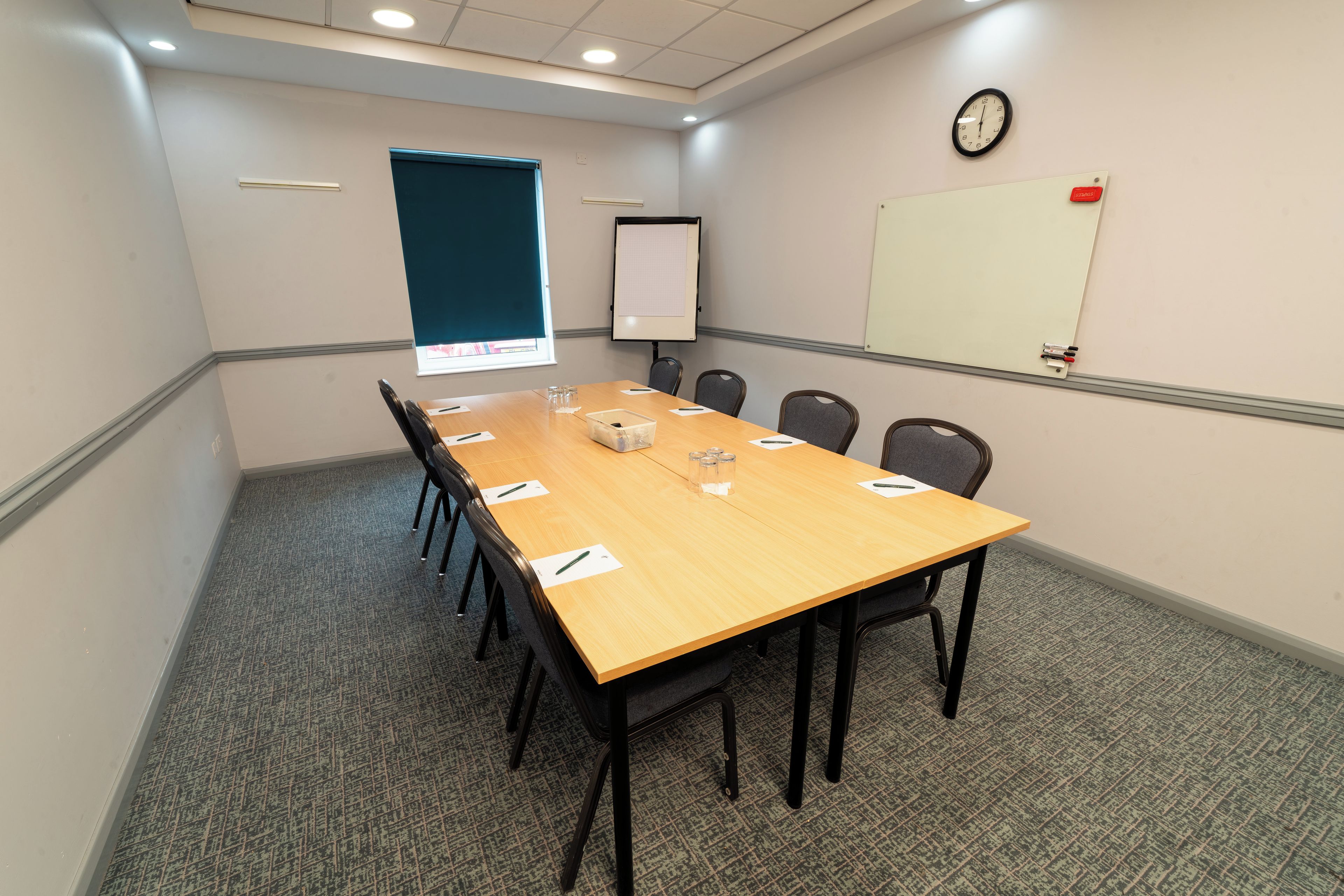 A conference room with a long table, chairs, a projector screen, a clock, and a whiteboard.
