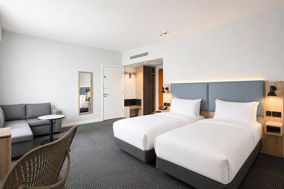 A hotel room with two beds, a sofa, a small table, a chair, and a mirror.
