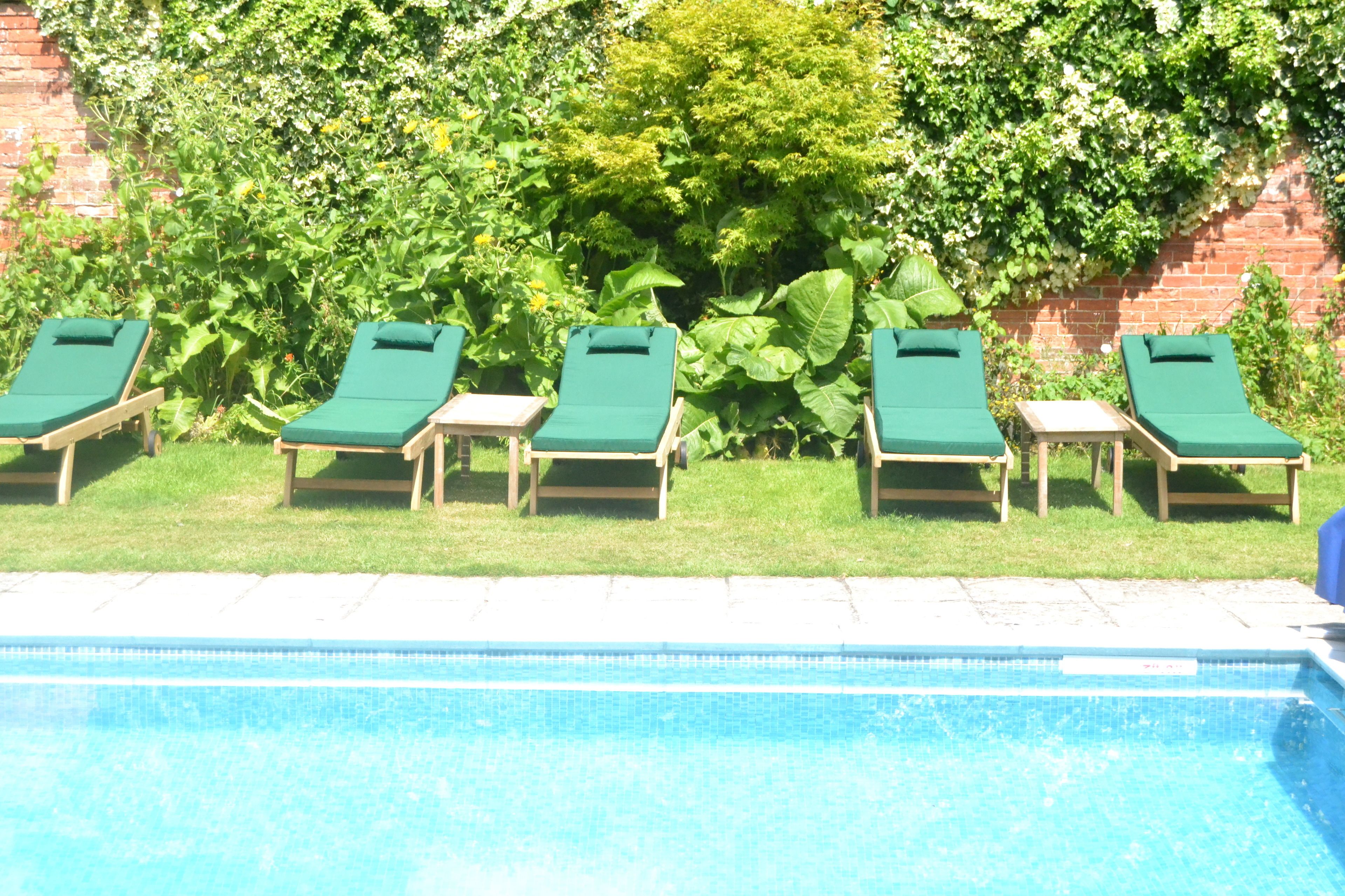 A pool area with four green lounge chairs aligned along the edge of a rectangular pool.