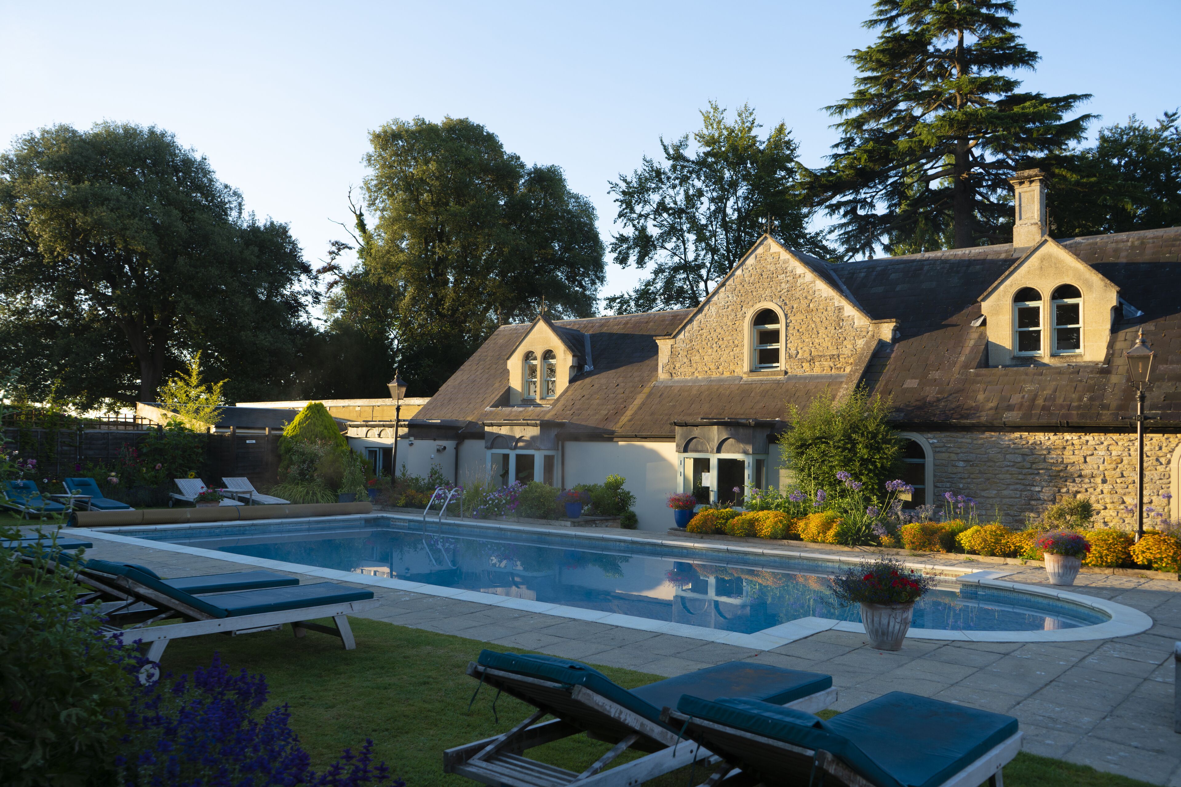 A pool area with lounge chairs and a stone building with a pitched roof.