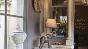 Une urne en marbre, une statue d’éléphant et une lampe posée sur un piédestal, dans une pièce bien éclairée, dotée de colonnes en pierre et d’une grande fenêtre.