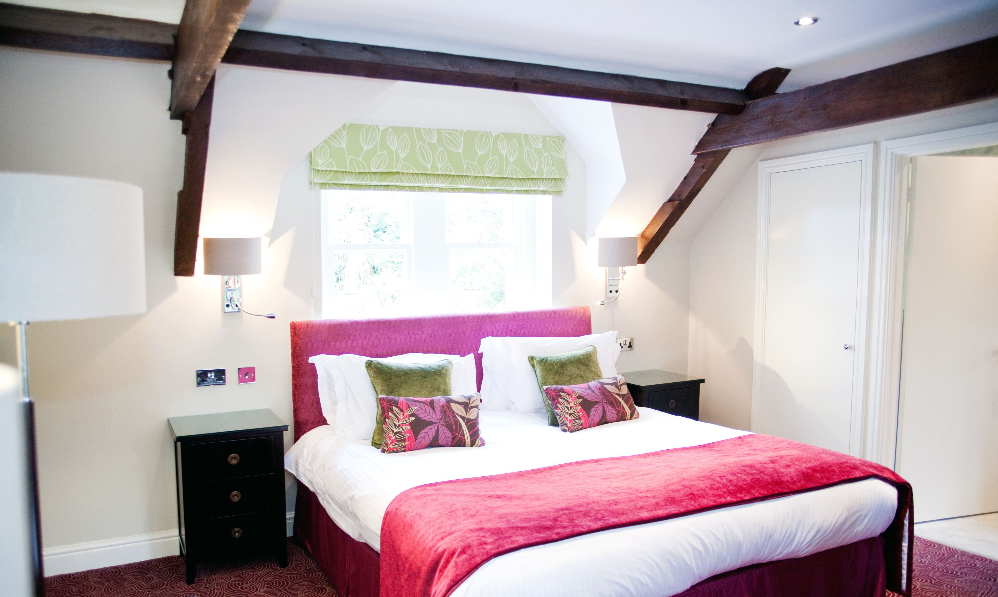 A bedroom with a bed, bedside tables, a window with a green valance, and a wardrobe.