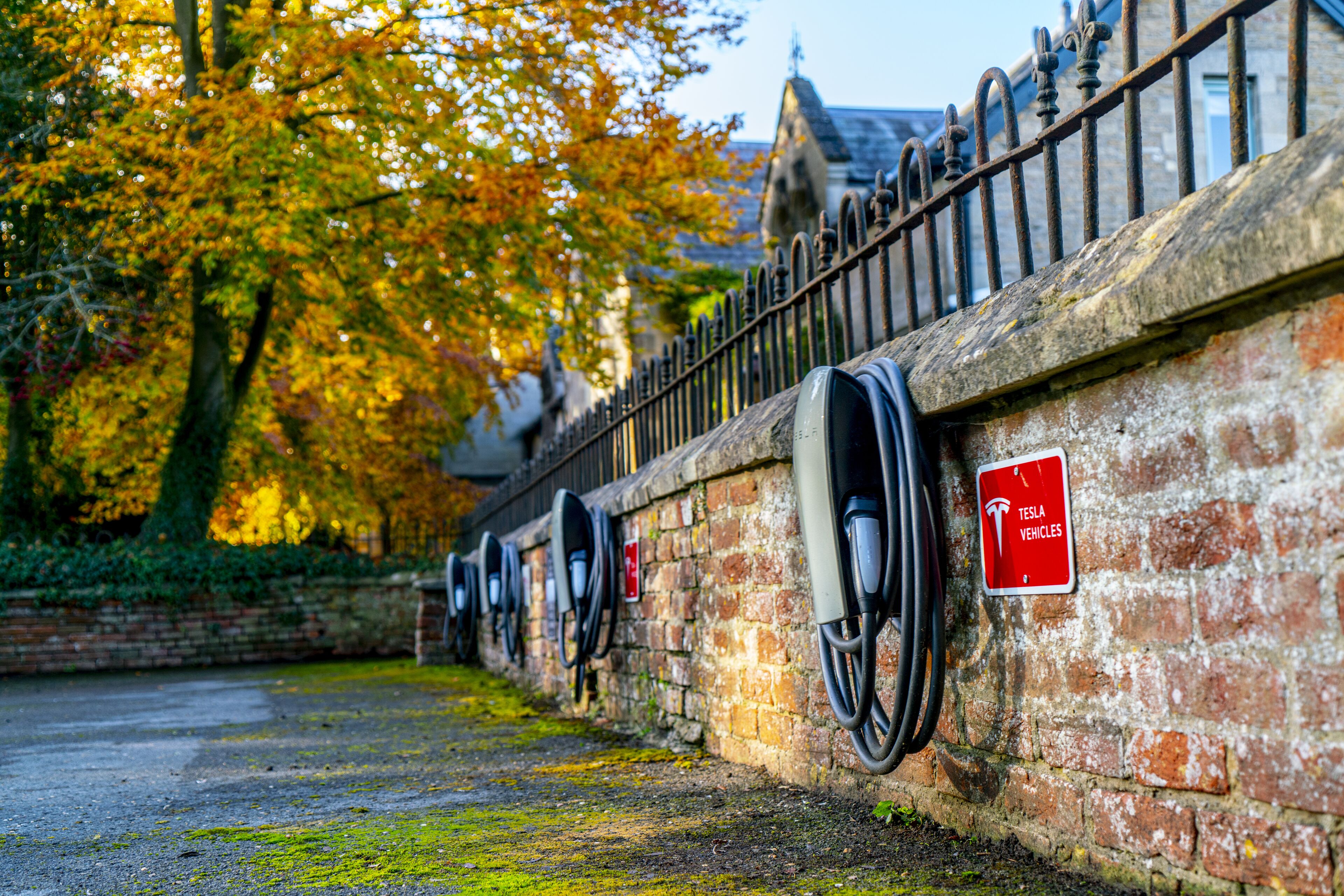 Une rangée de bornes de recharge pour véhicules électriques est fixée à un mur de briques, et une pancarte indique qu’elles sont réservées aux véhicules Tesla.