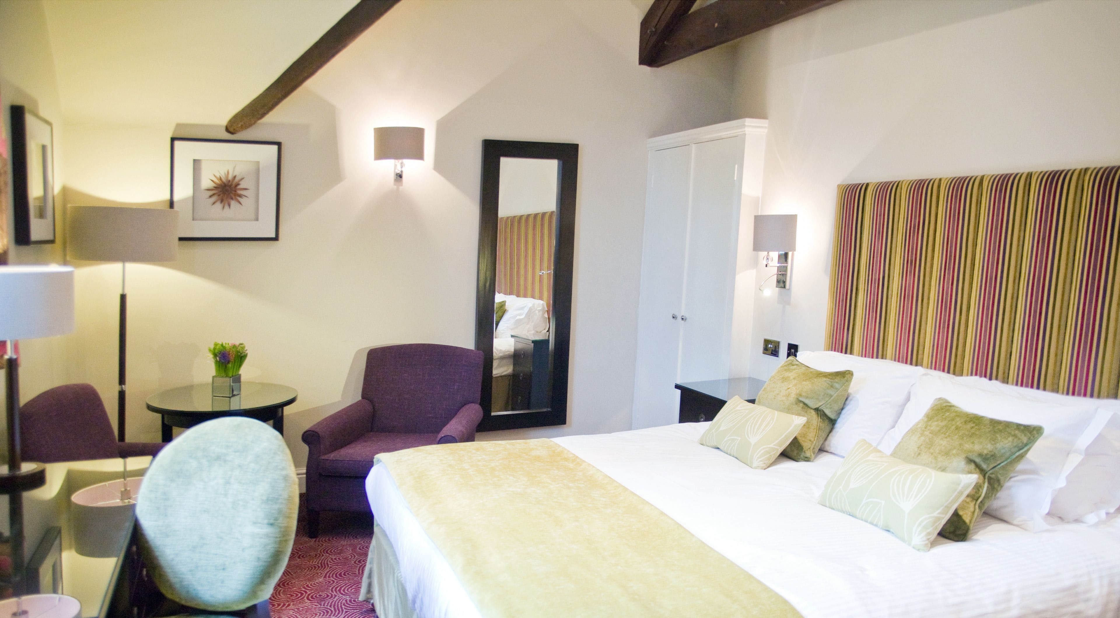 A hotel room with a bed, a chair, a desk, a mirror, and a lamp.