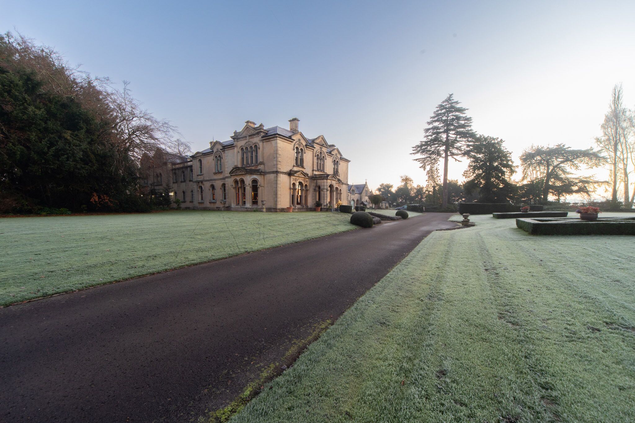 A large, historic building with a symmetrical facade, a paved pathway leading to it, and a well-maintained lawn.
