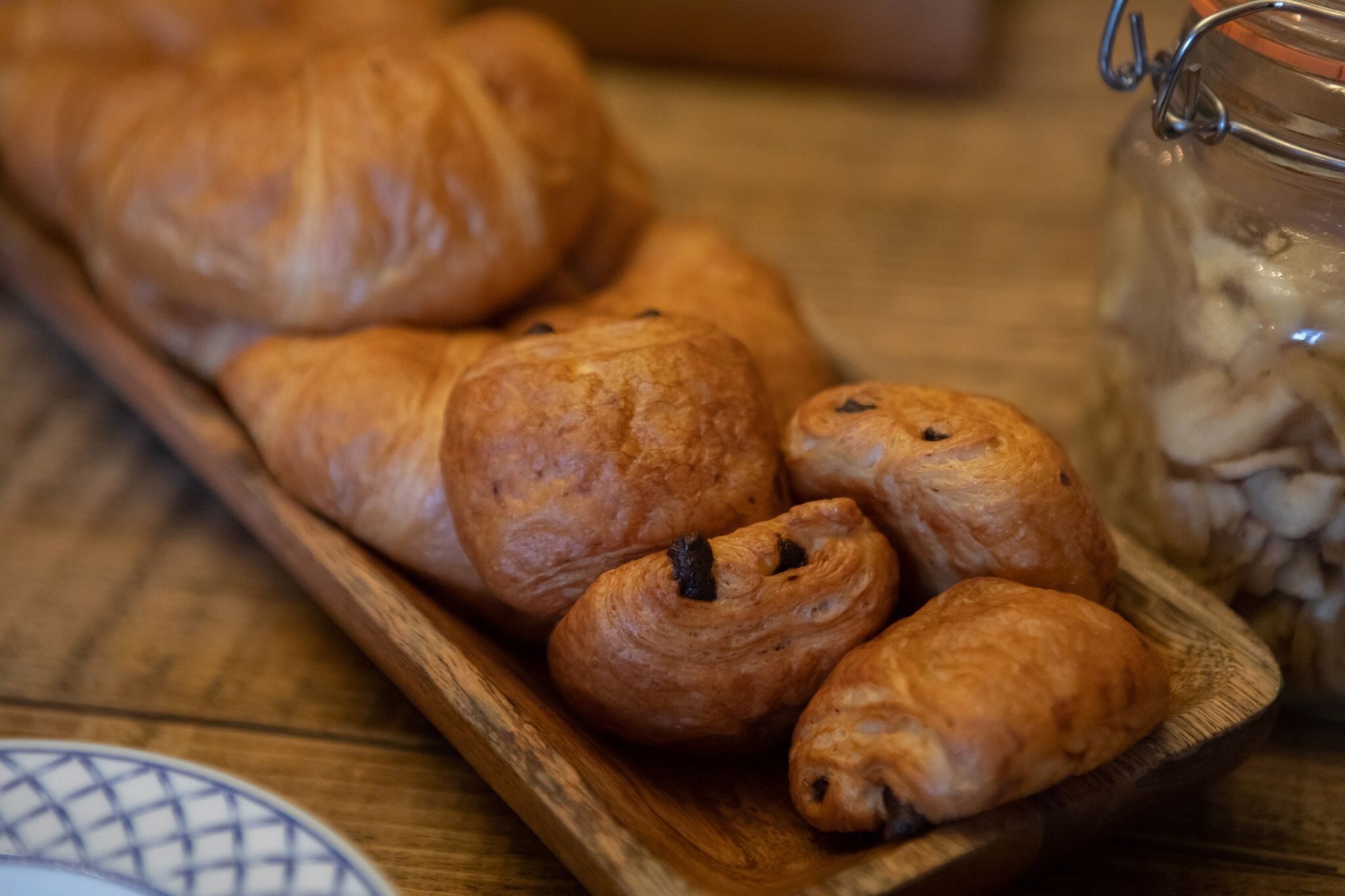 A wooden tray with several croissants and a jar of nuts.