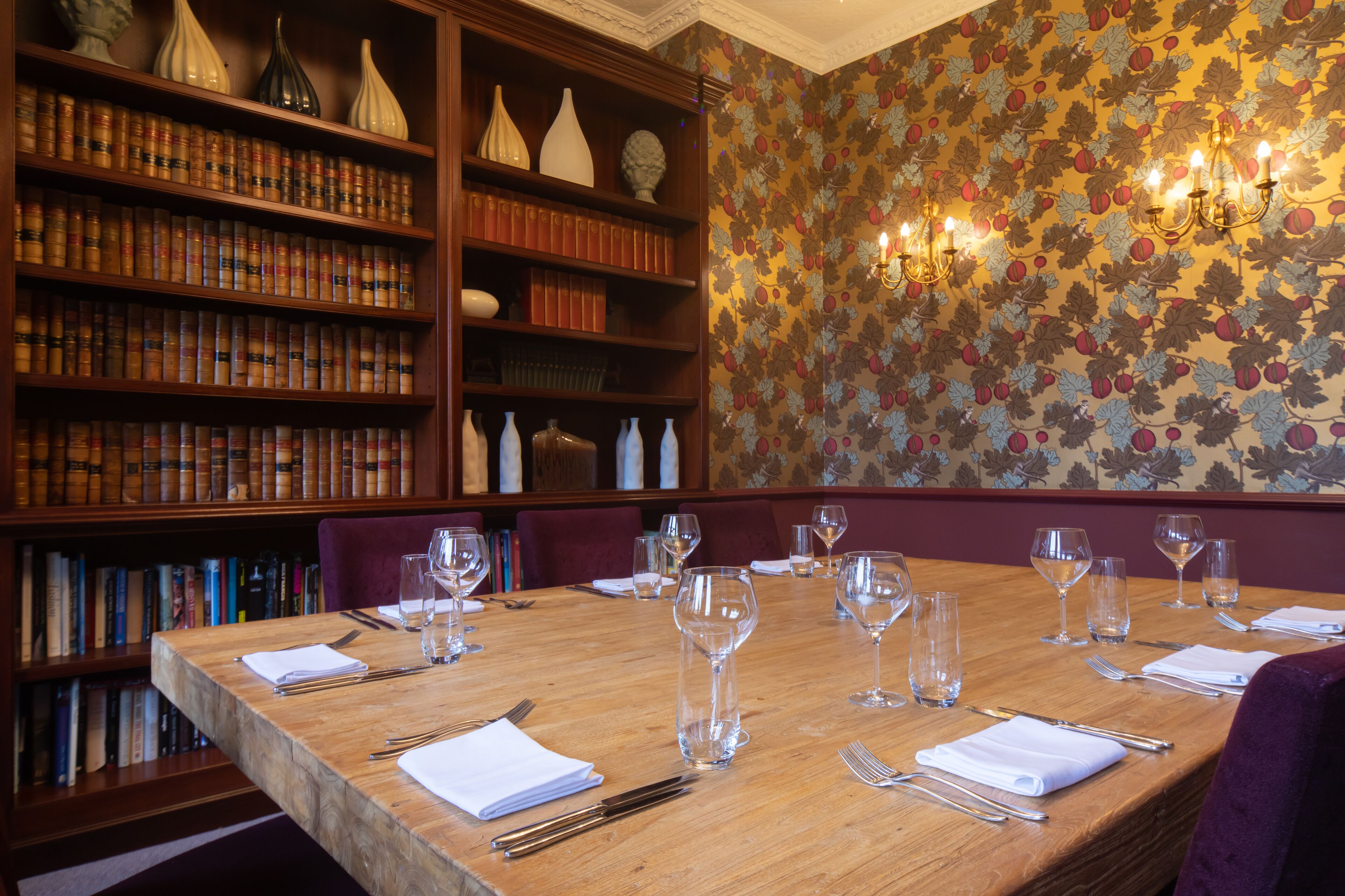 A dining table set for six with wine glasses and cutlery, surrounded by bookshelves filled with books and decorative items.