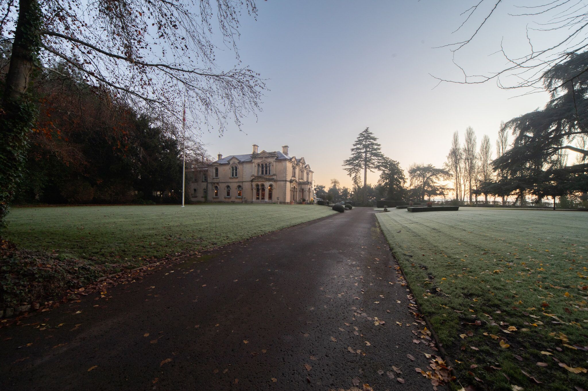 A pathway leading to a large, classical building with symmetrical architecture, surrounded by a well-maintained lawn and trees.