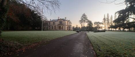 A pathway leading to a large, classical building with symmetrical architecture, surrounded by a well-maintained lawn and trees.