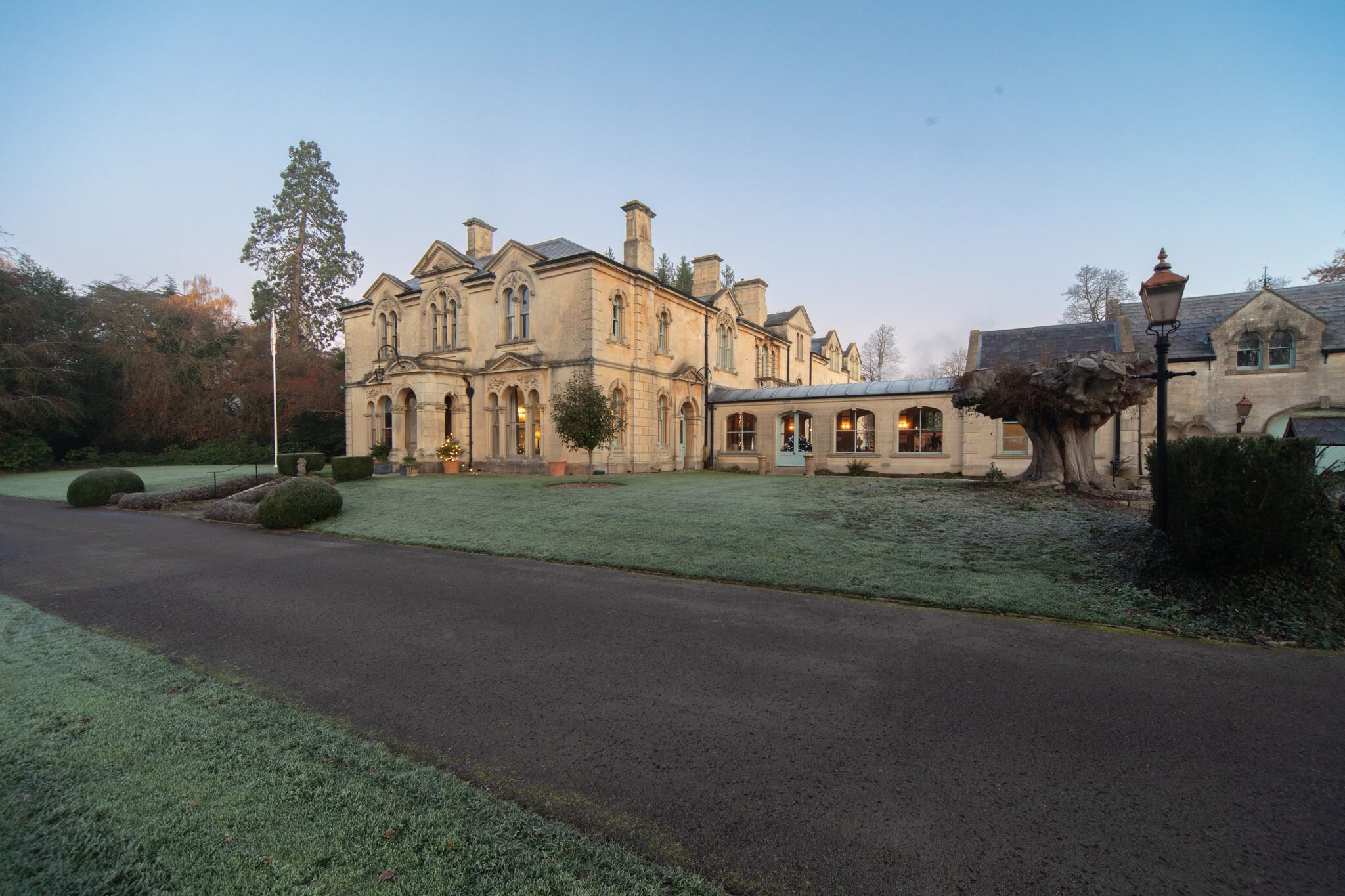 A large, historic building with multiple wings and arched windows, surrounded by a well-maintained lawn and a paved driveway.