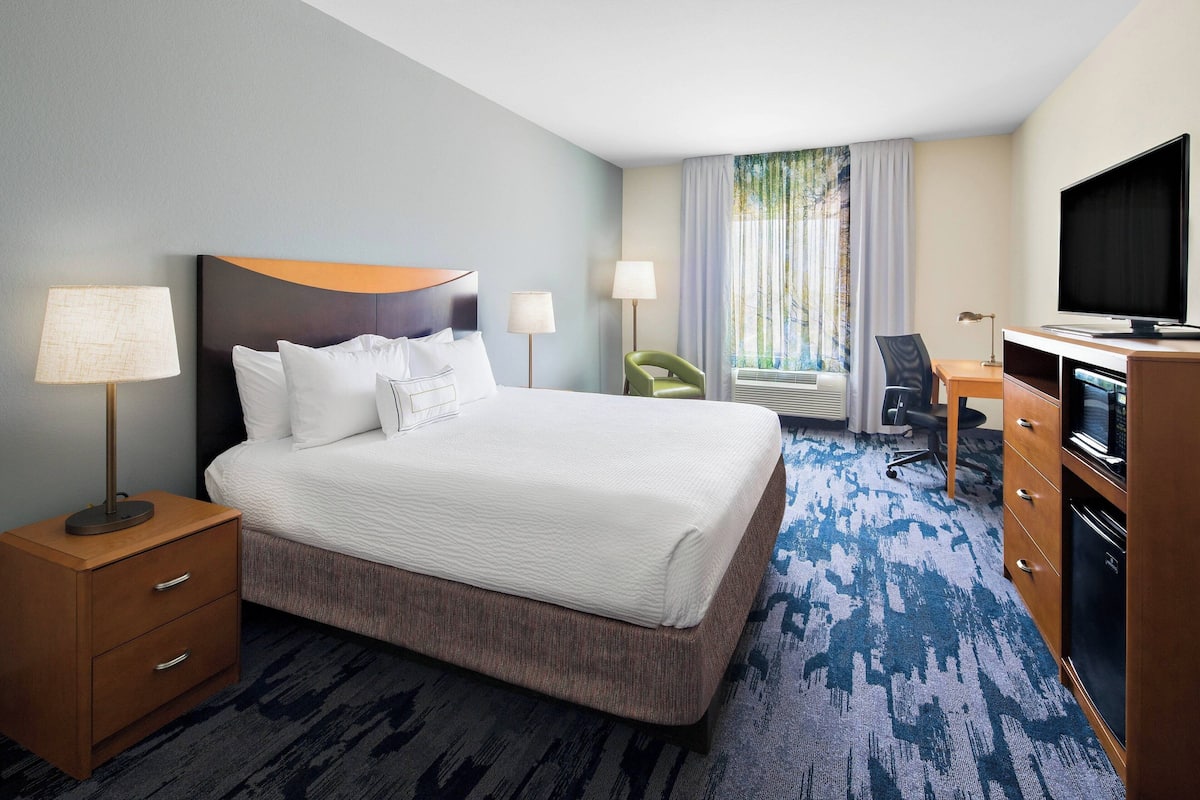 A hotel room with a large bed, a desk, a chair, a television, and a nightstand with lamps.