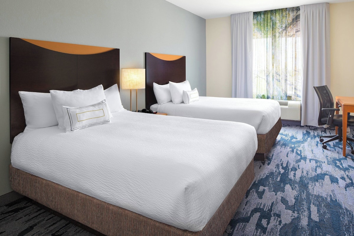 A hotel room with two beds, a desk, and a chair.