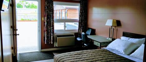 A hotel room with a bed, desk, chair, and a window with curtains.