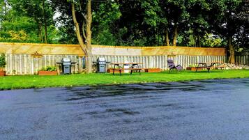 A fenced outdoor area with picnic tables and barbecue grills.