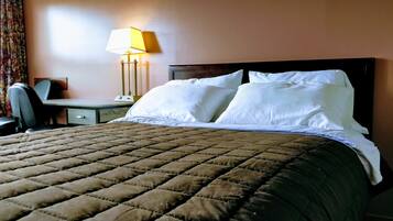 A hotel room with a large bed, a desk with a chair, and a lamp.