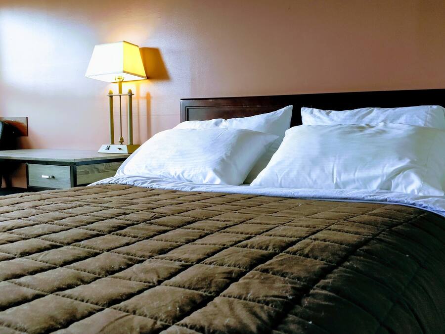 A hotel room with a large bed, a desk with a chair, and a lamp.