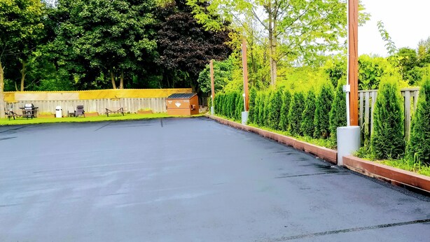 A parking area with a paved surface, a wooden fence, and a sign indicating video surveillance. - Kings Inn Midland (Midland)