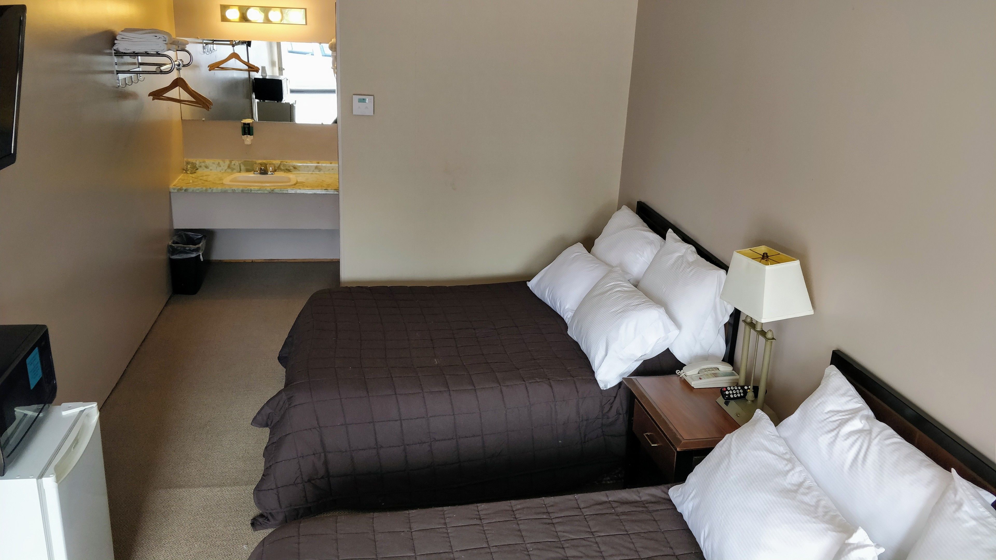 A hotel room with two beds, a bedside table with a lamp, a telephone, and a small table with a trash bin.