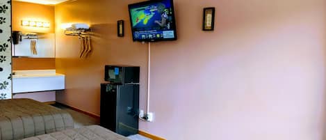 A hotel room with a bed, a TV mounted on the wall displaying a weather forecast, a sink, and a towel rack.