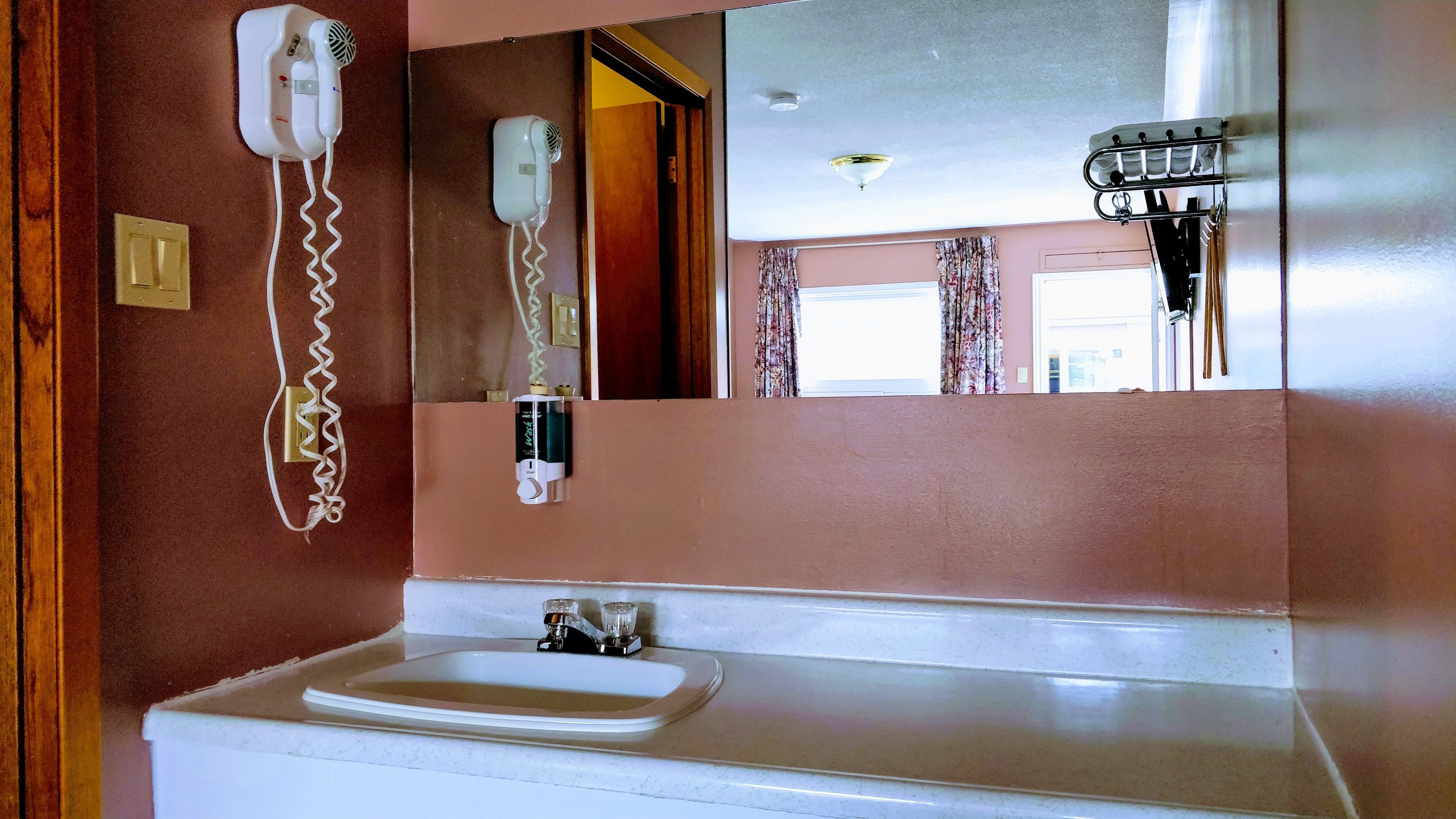 Un baño con un lavamanos blanco, un espejo y dos secadores de pelo fijados en la pared.