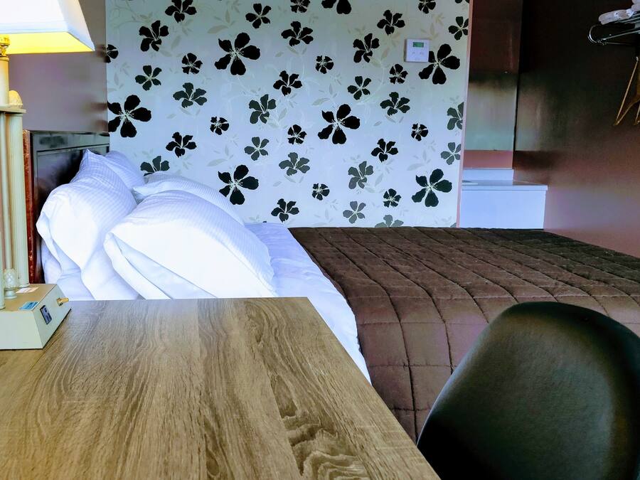 Quarto de hotel com cama, mesa de madeira, abajur e parede com padrão floral.