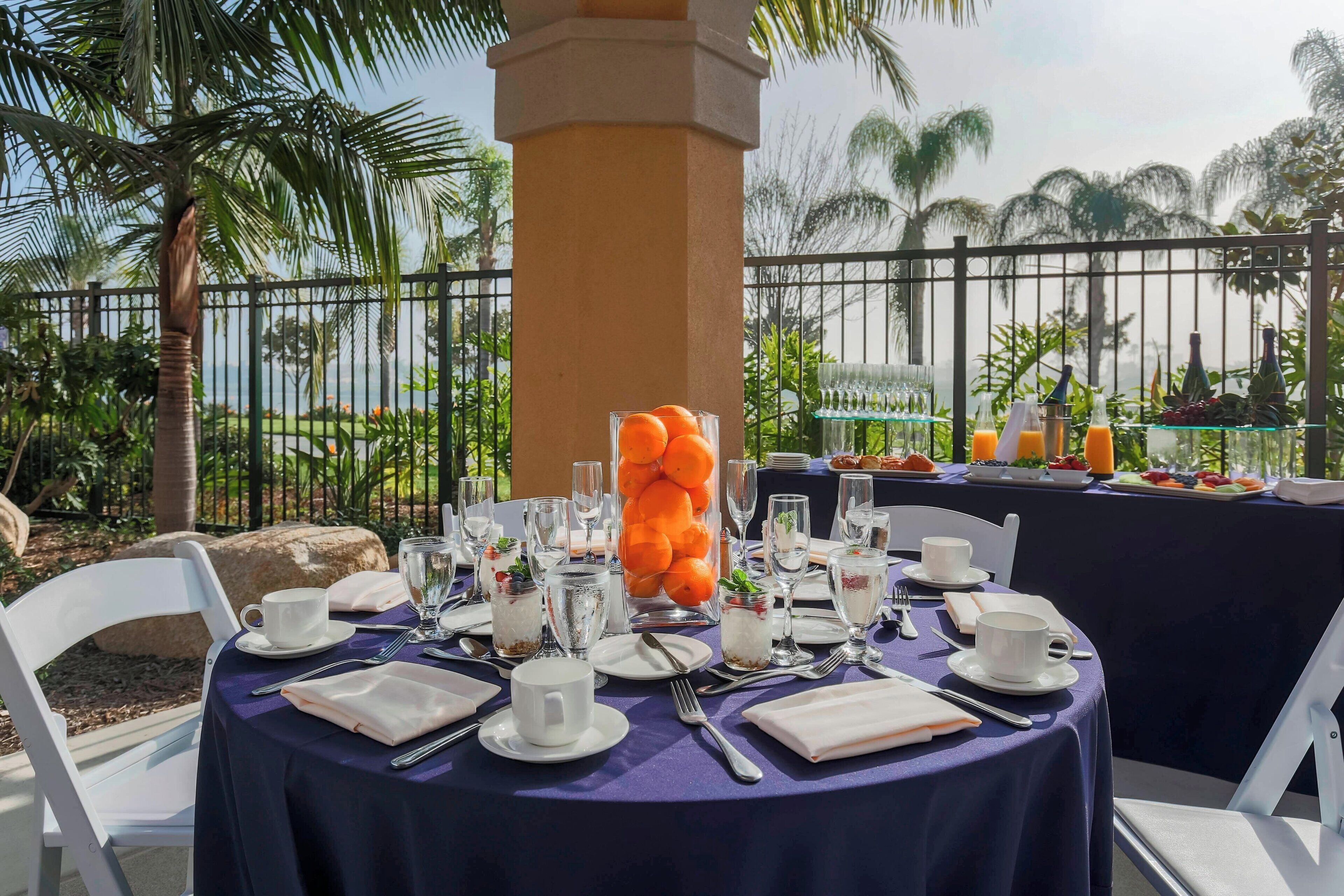 A table set for breakfast with a view of palm trees and a fence.