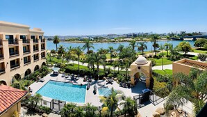 A resort with a swimming pool, lounge chairs, and a view of a lake and city skyline.