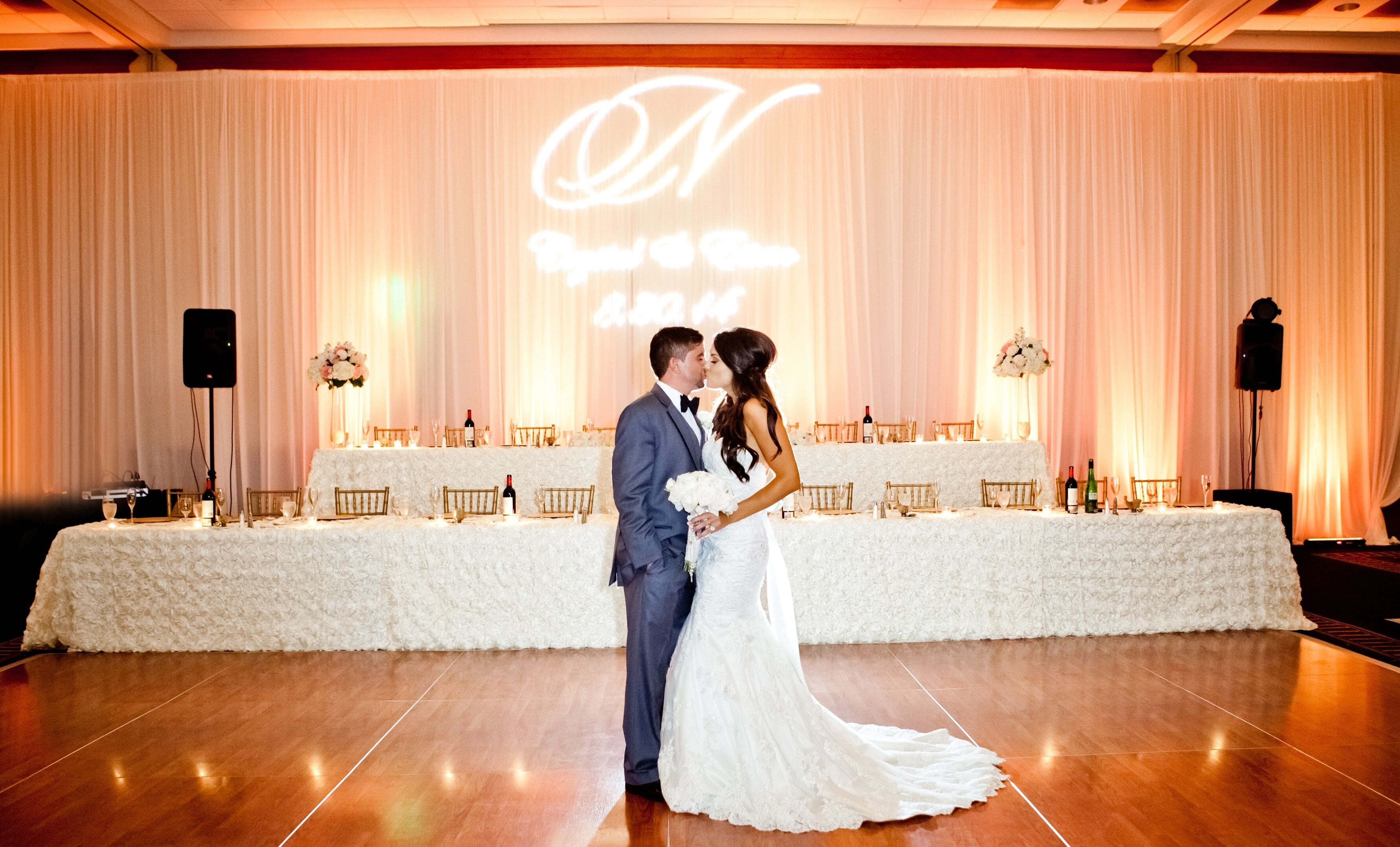 A wedding reception with a white table set against a backdrop with a projected 'N' and 'N' symbol.