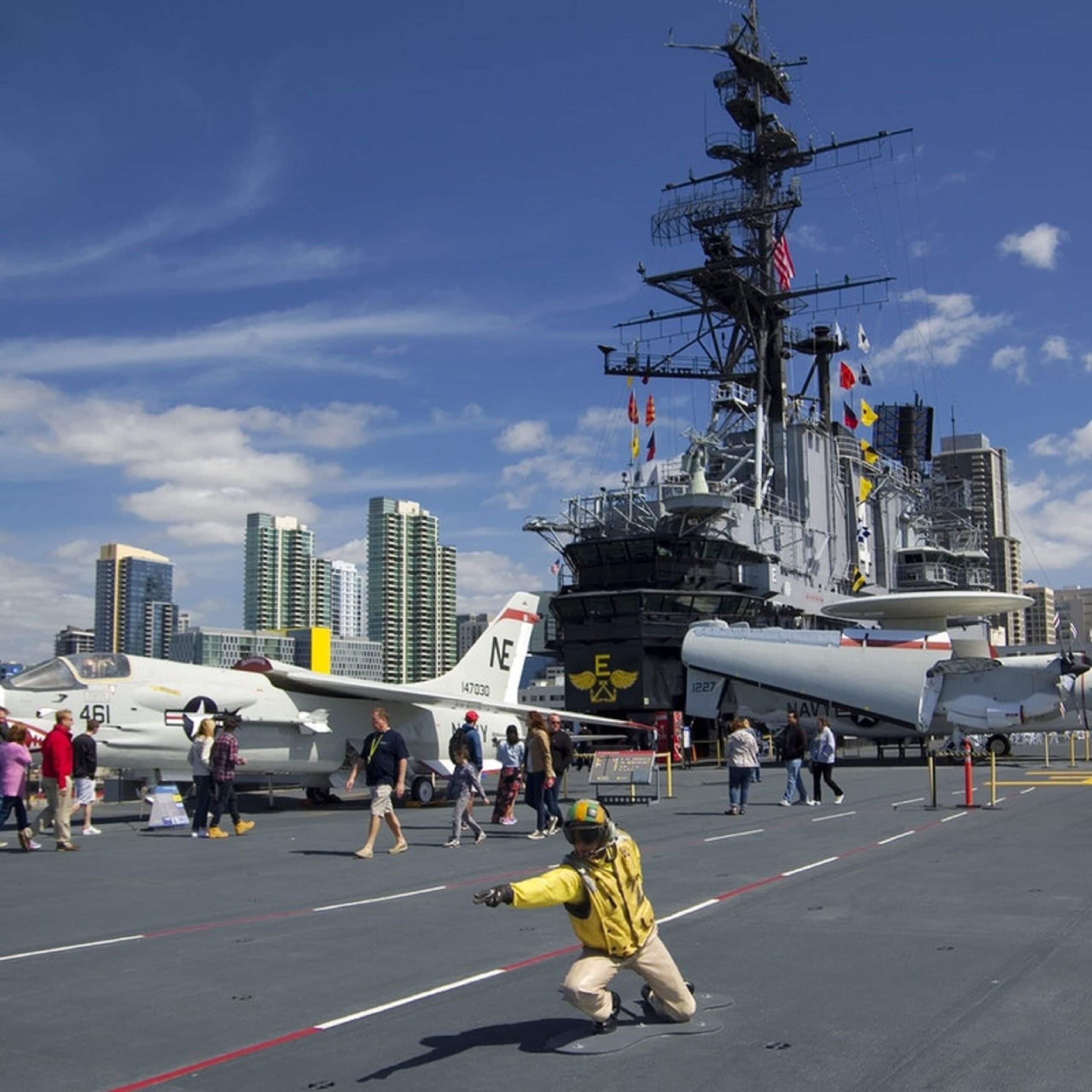 A naval aircraft carrier with multiple aircraft and personnel on deck.