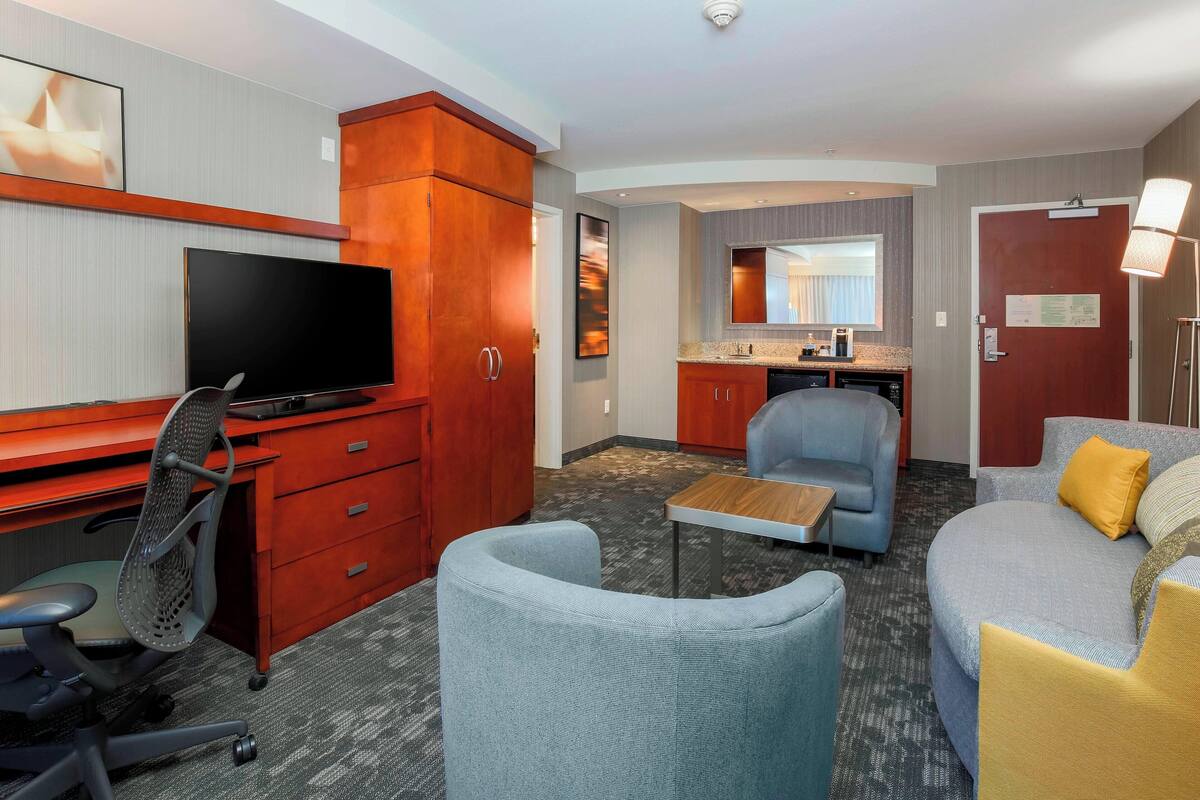 A hotel room with a TV, desk, office chair, sofa, and a small table.