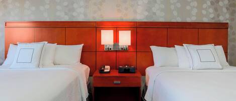 A hotel room with two beds, a wooden headboard, a nightstand with a phone and radio, and a patterned wallpaper.