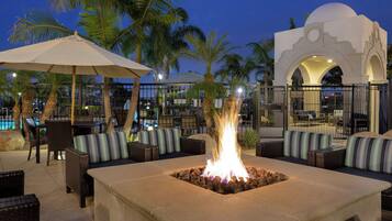 Un área de estar al aire libre con una chimenea, palmeras y una piscina al fondo.