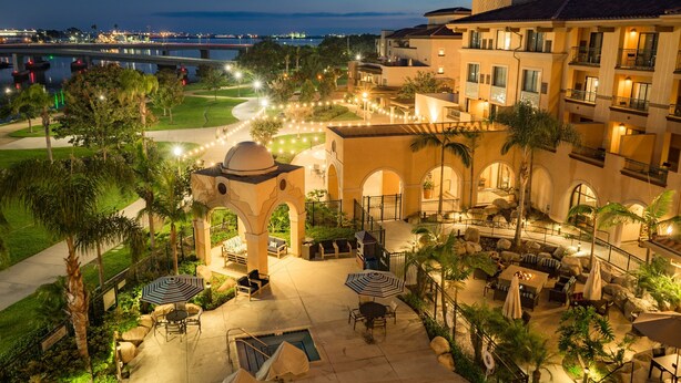 A hotel courtyard with outdoor seating, palm trees, and a view of the sea.