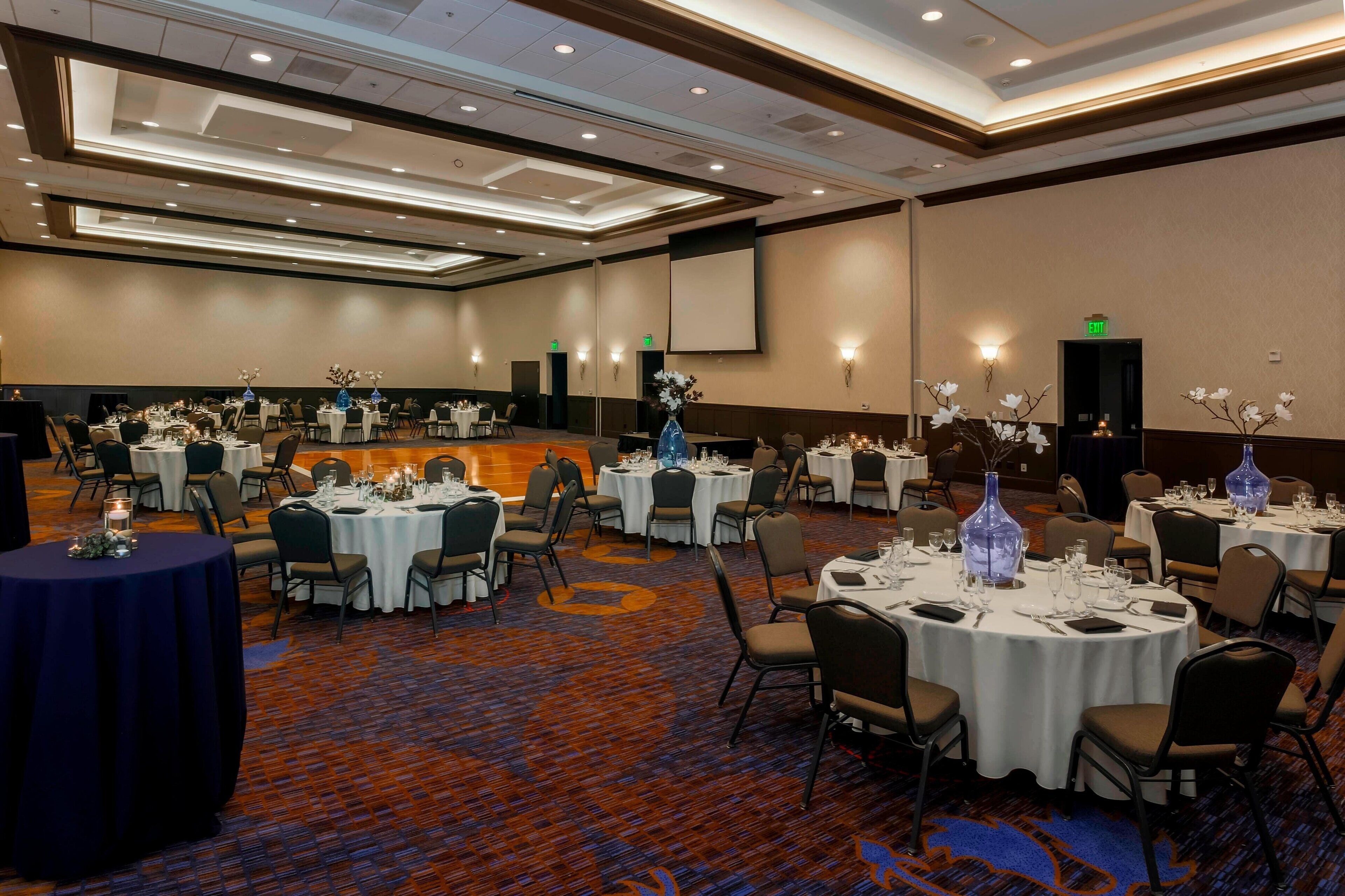 A banquet hall with round tables set for dining, equipped with candles and floral centerpieces.