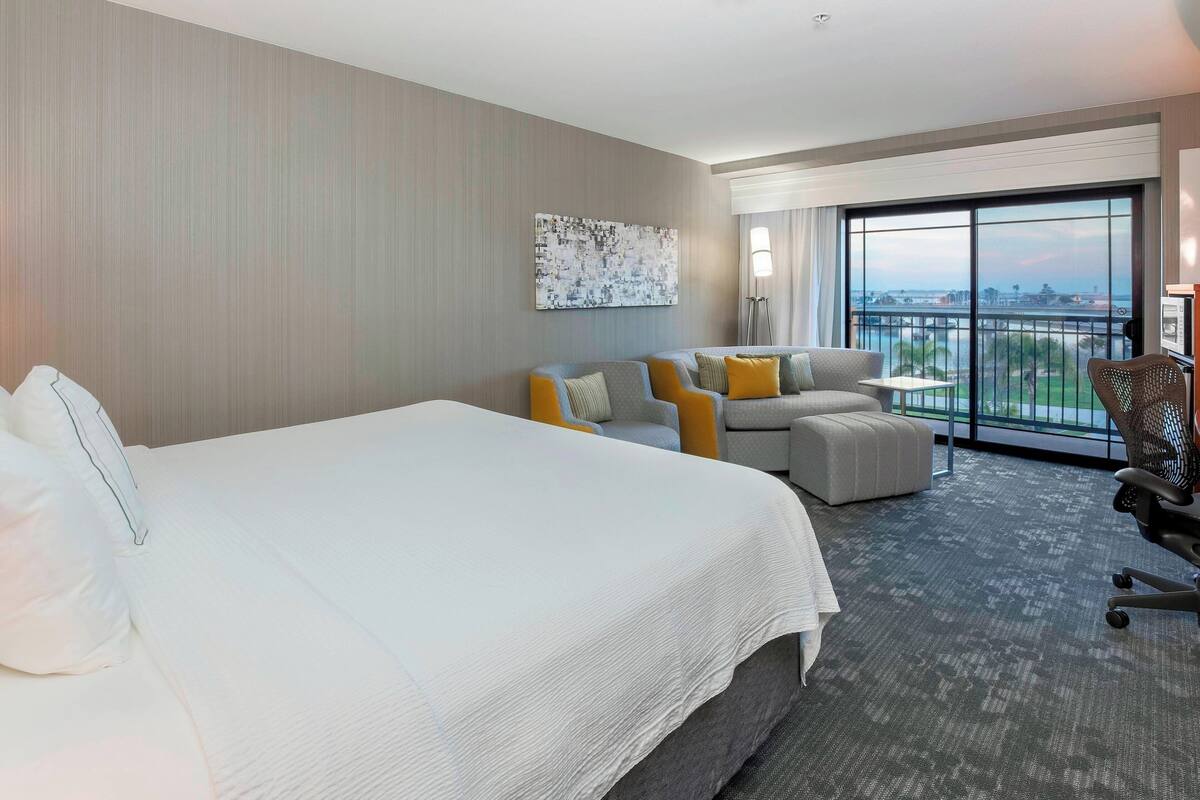 A hotel room with a large bed, a sofa, a chair, and a view of the city.