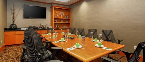 A conference room with a long table, black mesh chairs, and a TV mounted on the wall.