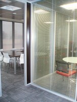 A conference room with a glass partition, white chairs, a round table, and a carpeted floor.
