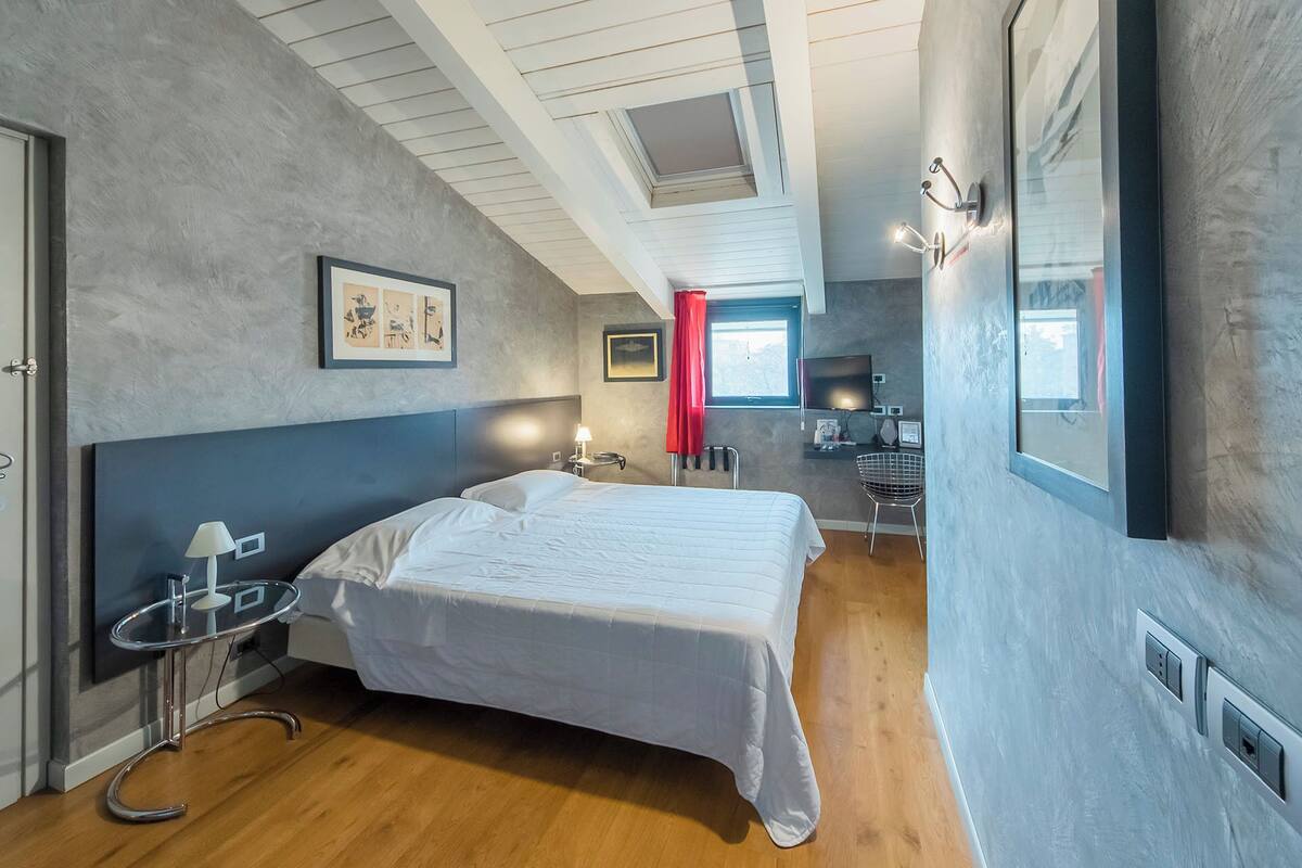 A modern bedroom with a large bed, a desk, and a window with red curtains.