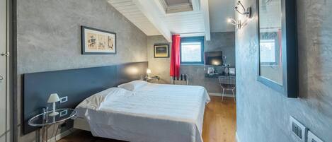 A modern bedroom with a large bed, a desk, and a window with red curtains.